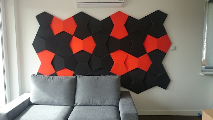 Dekoracyjna ściana z heksagonalnych paneli w kolorze czarnym i czerwonym nad szarą sofą w nowoczesnym wnętrzu.