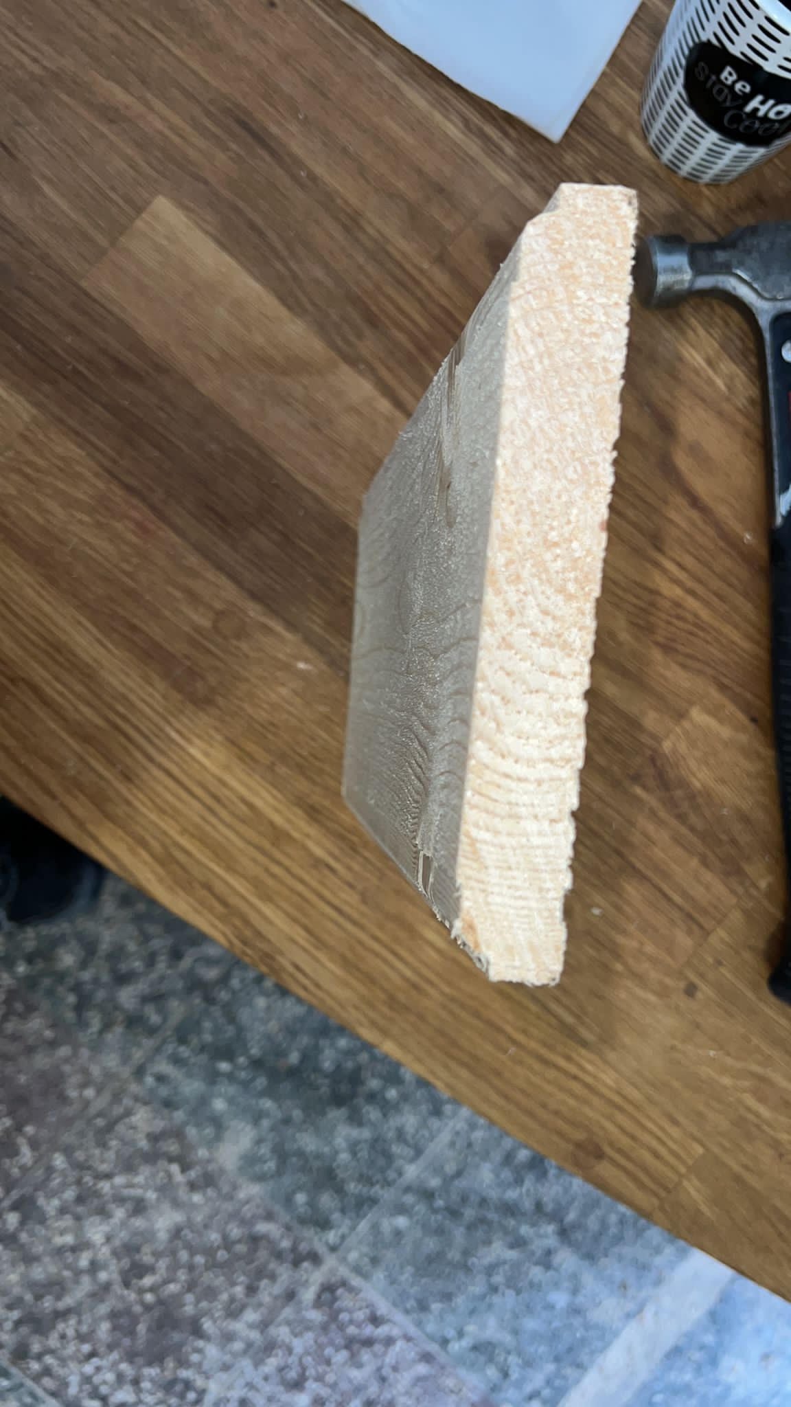 Przekrój deski boazeryjnej z widocznymi słojami drewna, leżącej na drewnianym blacie obok młotka i kubka.