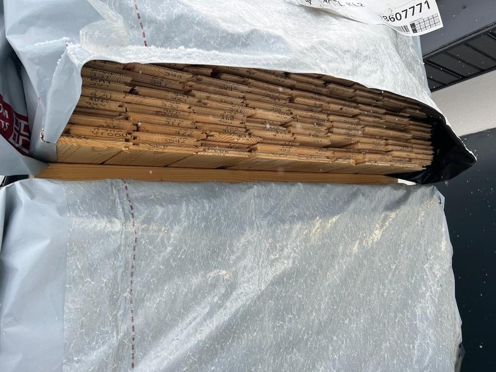 Stos drewnianych desek boazeryjnych w plastikowym opakowaniu, widoczne numery na każdej desce.