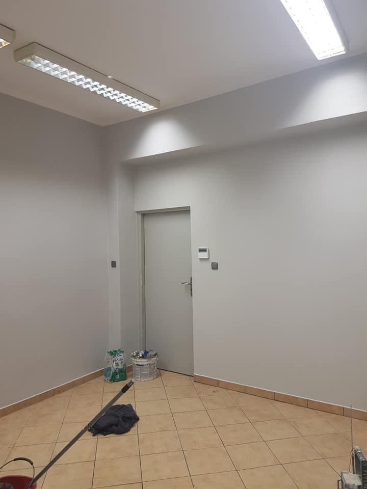 Wnętrze pomieszczenia po malowaniu ścian na szaro, widoczne wiadro z mopem, worki po farbie i drobne niedociągnięcia przy podłodze.