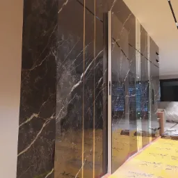 Ściana wykończona panelami imitującymi czarny marmur z białymi żyłami, oddzielonymi cienkimi złotymi paskami, z widoczną ochronną folią na podłodze.