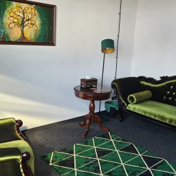 Libera Mentis - Marcin Żekoński - Gabinet psychoterapeutyczny z zielonymi, aksamitnymi meblami w stylu vintage, obrazem drzewa życia i zegarem na ścianie.