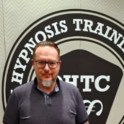 Portret mężczyzny w okularach na tle logotypu 'Hypnosis Training' w Chorzowie.