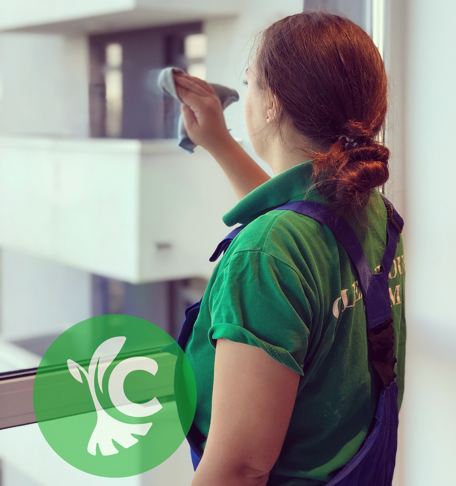 Kobieta w zielonej koszulce i granatowych ogrodniczkach czyści okno szmatką, widoczny fragment logo firmy na koszulce.