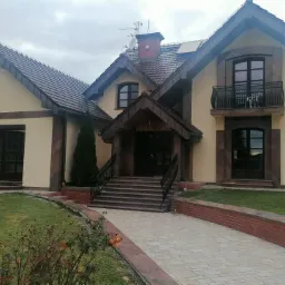 Elewacja dwukondygnacyjnego domu z ciemnymi ramami okiennymi i roletami zewnętrznymi, widok z przodu, pochmurne niebo.