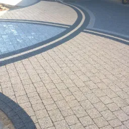 Nowa nawierzchnia z kostki brukowej w odcieniach beżu i szarości, ułożona w łukowaty wzór z ciemnymi obramowaniami, widoczne przygotowane podłoże.