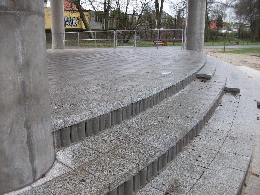 Szara, granitowa nawierzchnia placu z kolumnami i schodami, widok z dołu. Charakterystyczna faktura kostki i precyzyjne wykonanie. Detale architektoniczne.