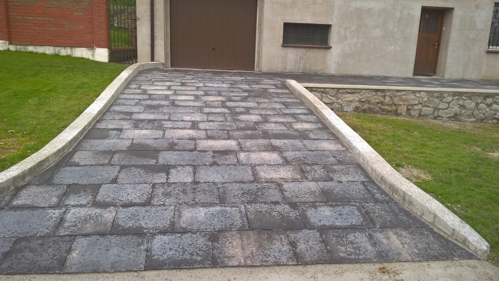 Podjazd z kostki brukowej we Wrocławiu, wykończony betonowymi obrzeżami, prowadzący do garażu. Widoczne fragmenty trawnika i elewacji budynku.
