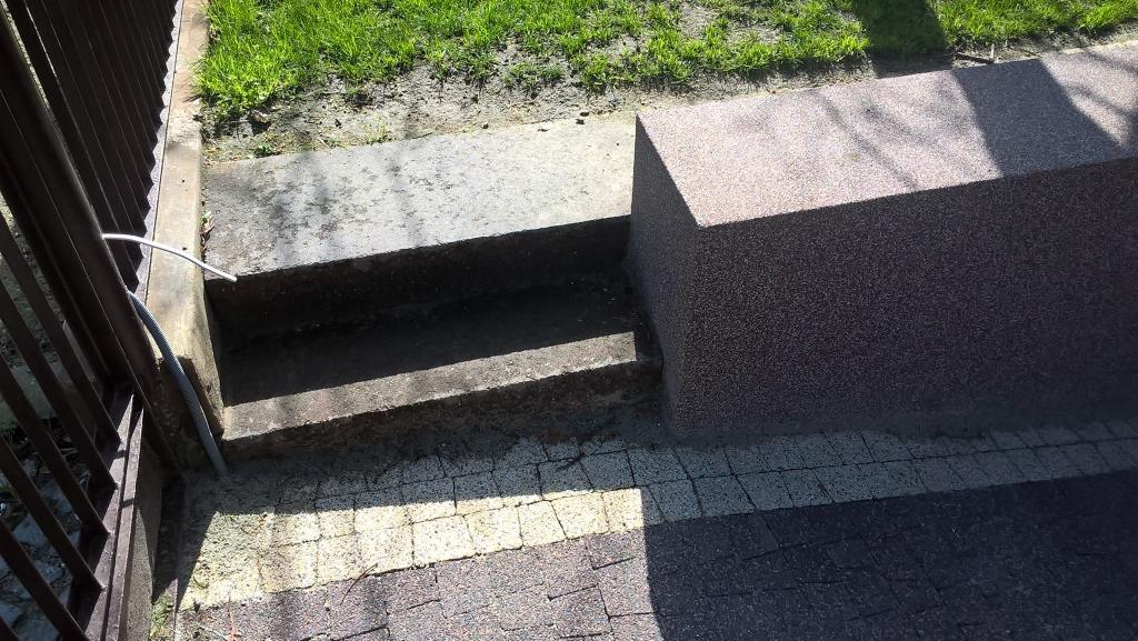 Schody z kostki brukowej prowadzące do ogrodu, obok metalowe ogrodzenie i trawnik. Widoczne detale wykończenia i kolorystyka kostki.