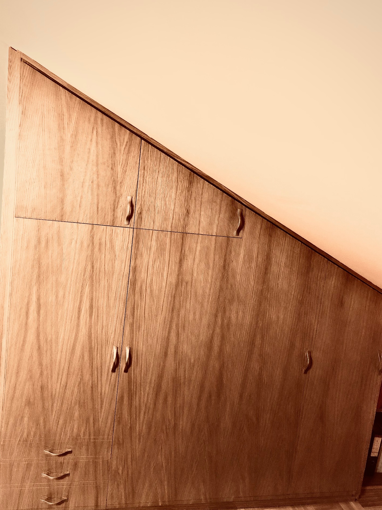 Drewniana szafa na wymiar, zabudowa pod skosem dachu, z uchwytami i trzema szufladami na dole.