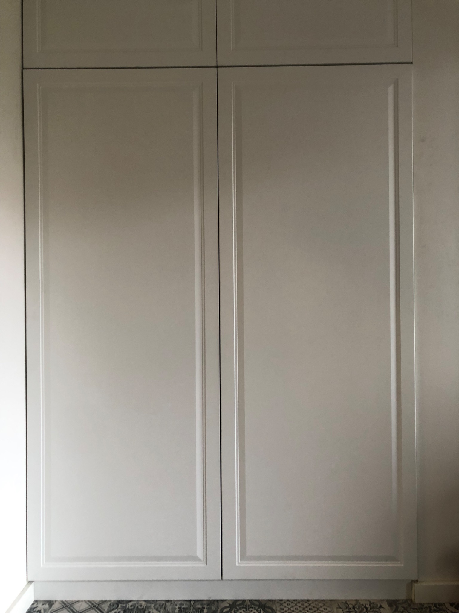 Biała szafa wnękowa z frezowanymi drzwiami i dekoracyjną podłogą z płytek.