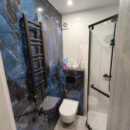 WOJBUD Firma Ogólnobudowlana - Nowoczesna łazienka z płytkami imitującymi marmur w odcieniach błękitu i złota, czarnym grzejnikiem drabinkowym i kabiną prysznicową z czarnymi profilami.