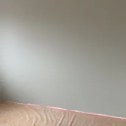 Świeżo pomalowana ściana w odcieniach zieleni, zabezpieczona folią podłoga z widocznymi śladami farby, listwa przypodłogowa odcięta taśmą malarską.