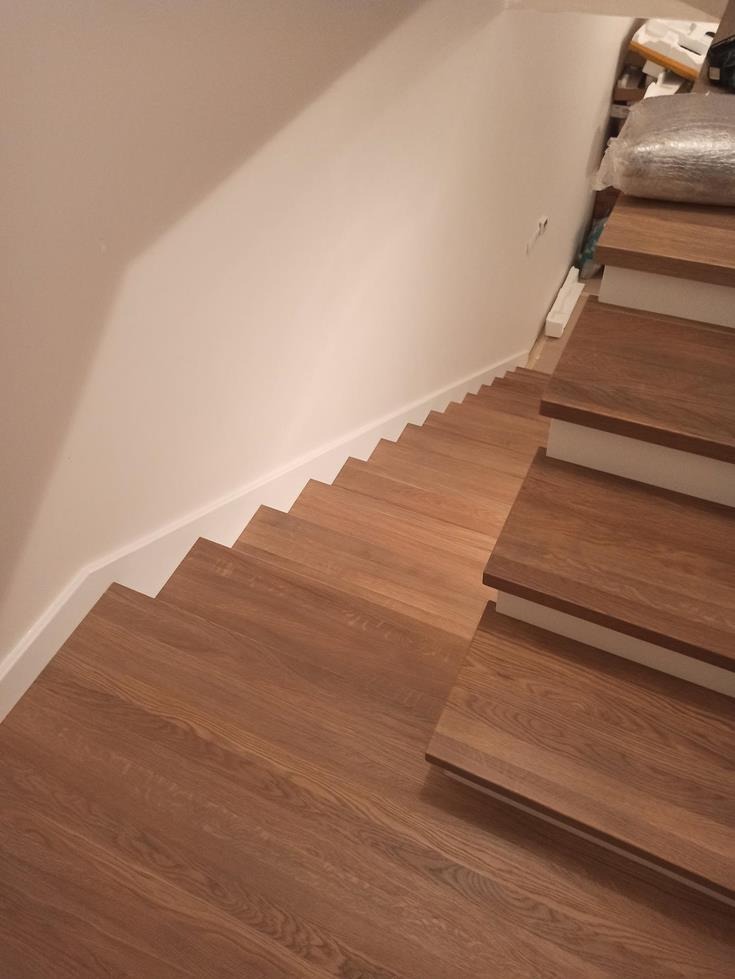 Nowoczesne, drewniane schody z białymi podstopnicami, widok z góry, widoczne materiały budowlane na górze schodów.