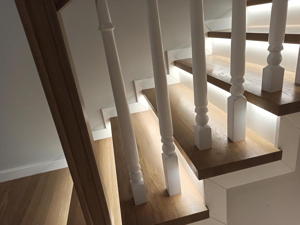 Nowoczesne schody z drewnianymi stopniami i białymi balustradami, podświetlone od spodu diodami LED, widok z dołu.