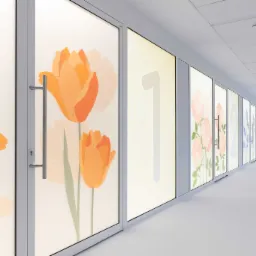 Długi korytarz biurowy z przeszklonymi drzwiami, na kt&oacute;rych umieszczono grafiki kwiatowe i numeryczne, tworząc estetyczny system identyfikacji wizualnej.