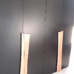 Czarna szafa z drewnianymi, falowanymi uchwytami na tle jasnej podłogi.