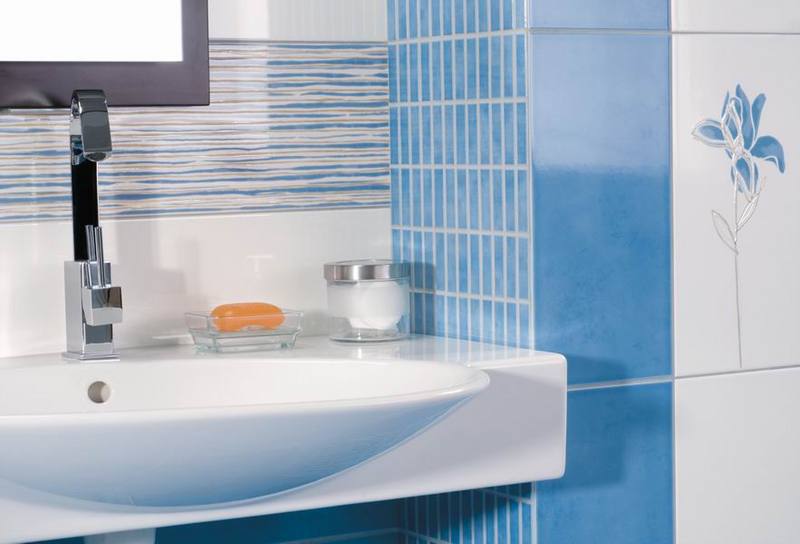Nowoczesna łazienka z białą umywalką, chromowaną baterią i niebiesko-białymi płytkami z motywem kwiatowym, uzupełniona akcesoriami łazienkowymi.
