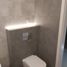 ADBUD Adam Bałdowski - Nowoczesna toaleta podwieszana z szarymi płytkami i podświetleniem LED nad zabudową stelaża.