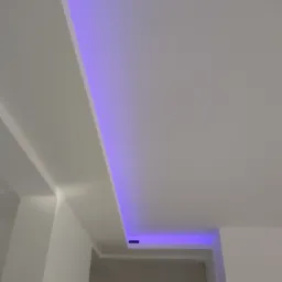 Biały sufit z wbudowanym oświetleniem LED w kolorze fioletowym, widok z dołu, fragment korytarza w tle.