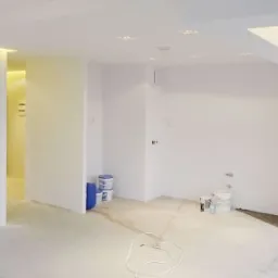 Wnętrze w trakcie remontu w Sierakowicach: białe ściany, sufit z oświetleniem punktowym i dekoracyjnym, widoczne puszki z farbą i kabel na podłodze.