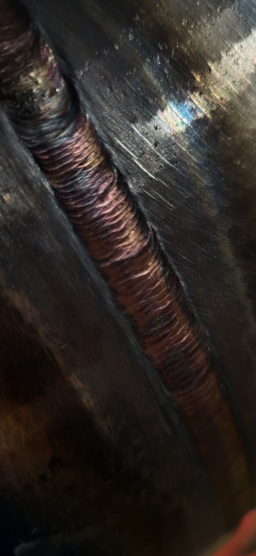 Spoina o nieregularnej fakturze i opalizującym zabarwieniu na metalowej powierzchni z widocznymi śladami szlifowania.