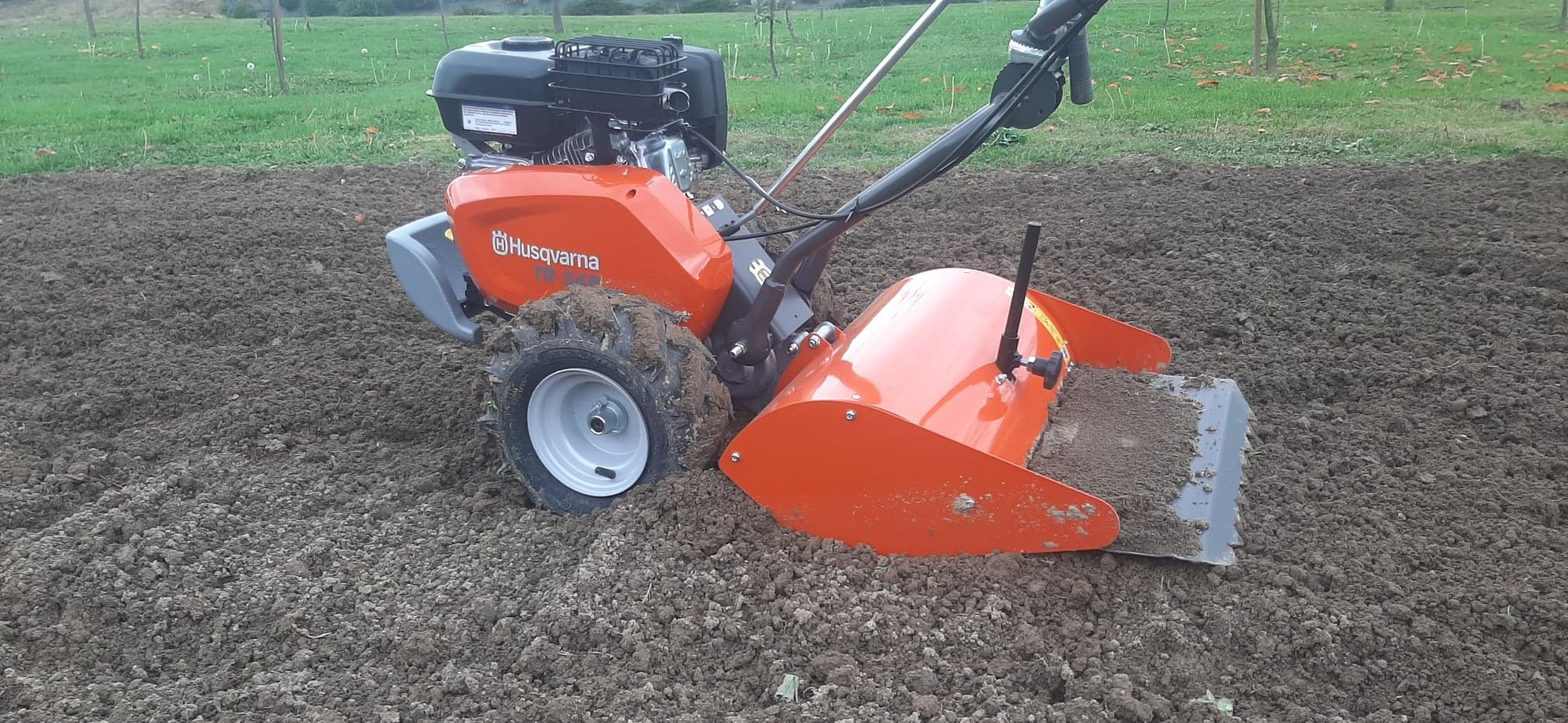 Pomarańczowy glebogryzarka Husqvarna TX 300 w trakcie pracy na polu, widoczne świeżo spulchnione grudy ziemi.