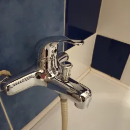 Błyszcząca, chromowana bateria wannowa z wężem prysznicowym na tle niebiesko-białej glazury w łazience.