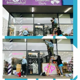 Pracownicy na drabinach myją duże okna witrynowe sklepu z balonami i kostiumami, widoczne logo 'kostiumowo.pl' i 'Balloon Bar' nad wejściem.