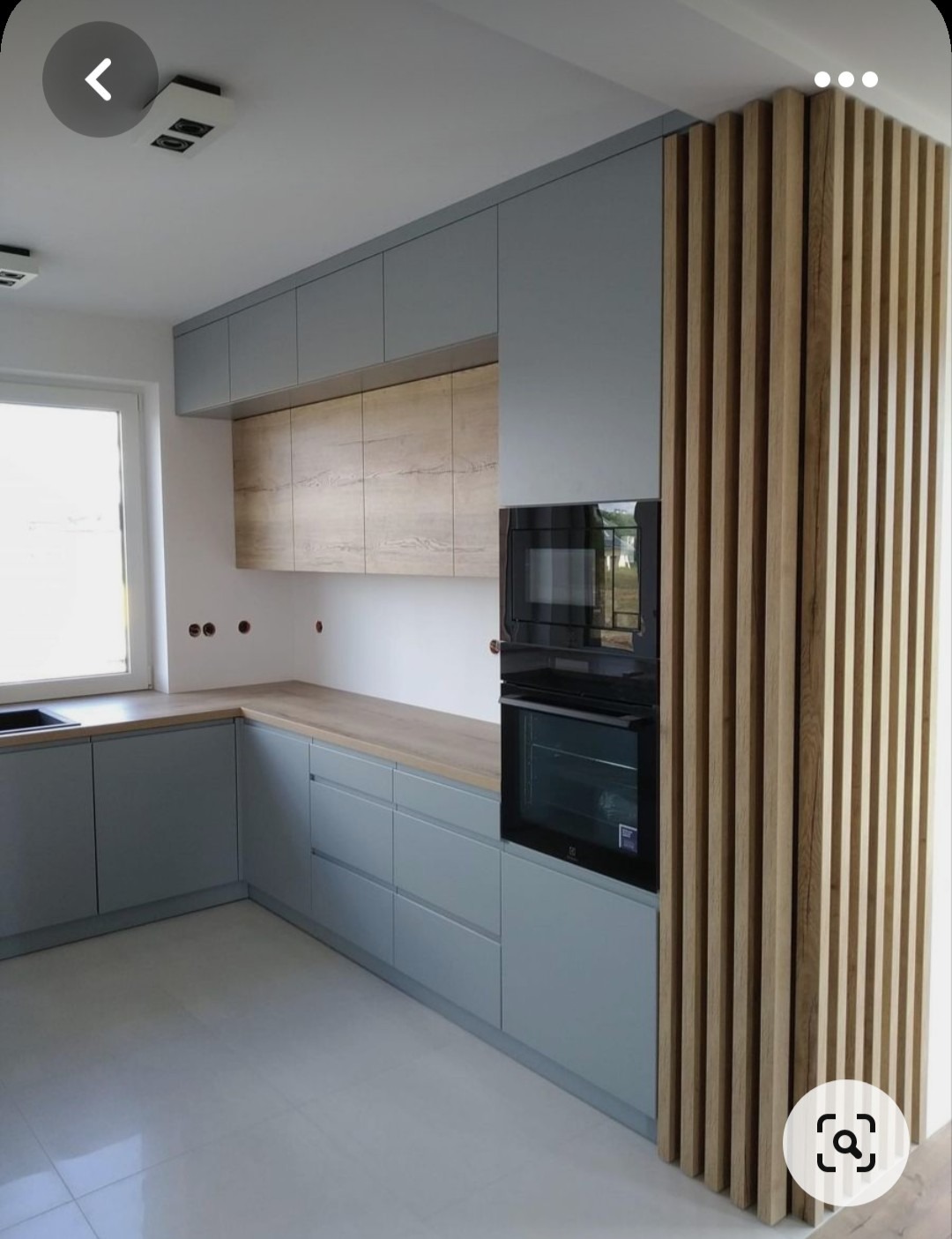 Nowoczesna kuchnia z szarymi szafkami, drewnianym blatem i dekoracyjnymi drewnianymi listwami pionowymi po prawej stronie, z wbudowanym piekarnikiem elektrycznym.