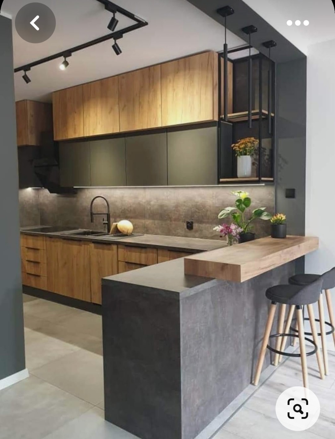 Nowoczesna kuchnia z drewnianymi frontami szafek górnych i oliwkowymi dolnymi, szary blat, wyspa z blatem barowym i hokerami, oświetlenie punktowe na szynie