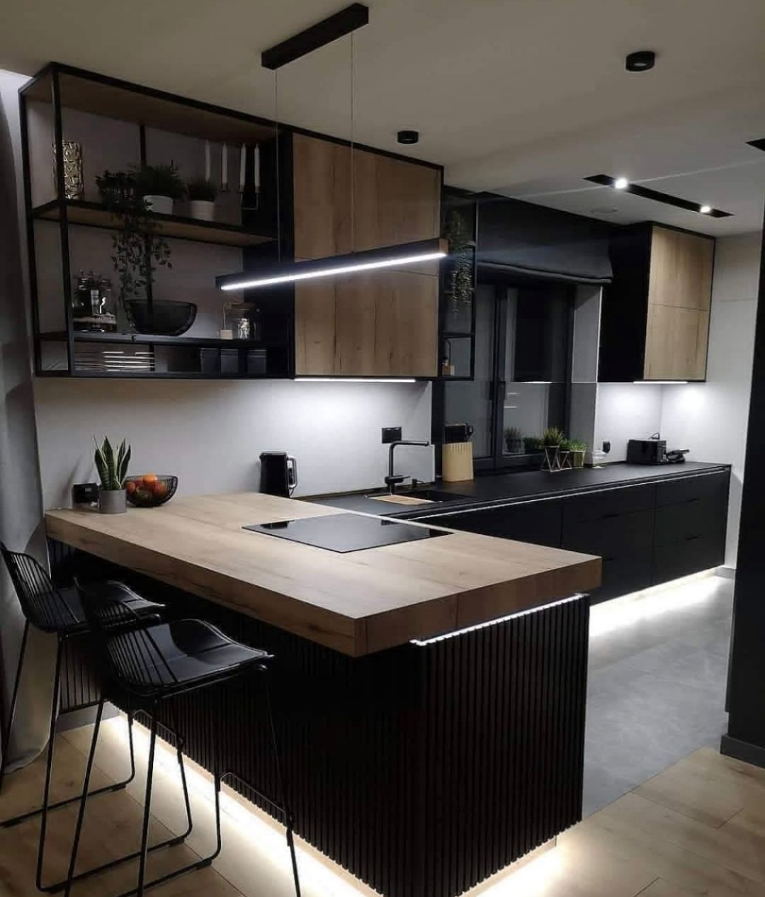 Nowoczesna kuchnia z wyspą: czarne szafki dolne, drewniane szafki górne i blat wyspy z ukrytą płytą grzewczą, oświetlenie LED pod szafkami i wyspą, minimalistyczne czarne krzesła barowe.