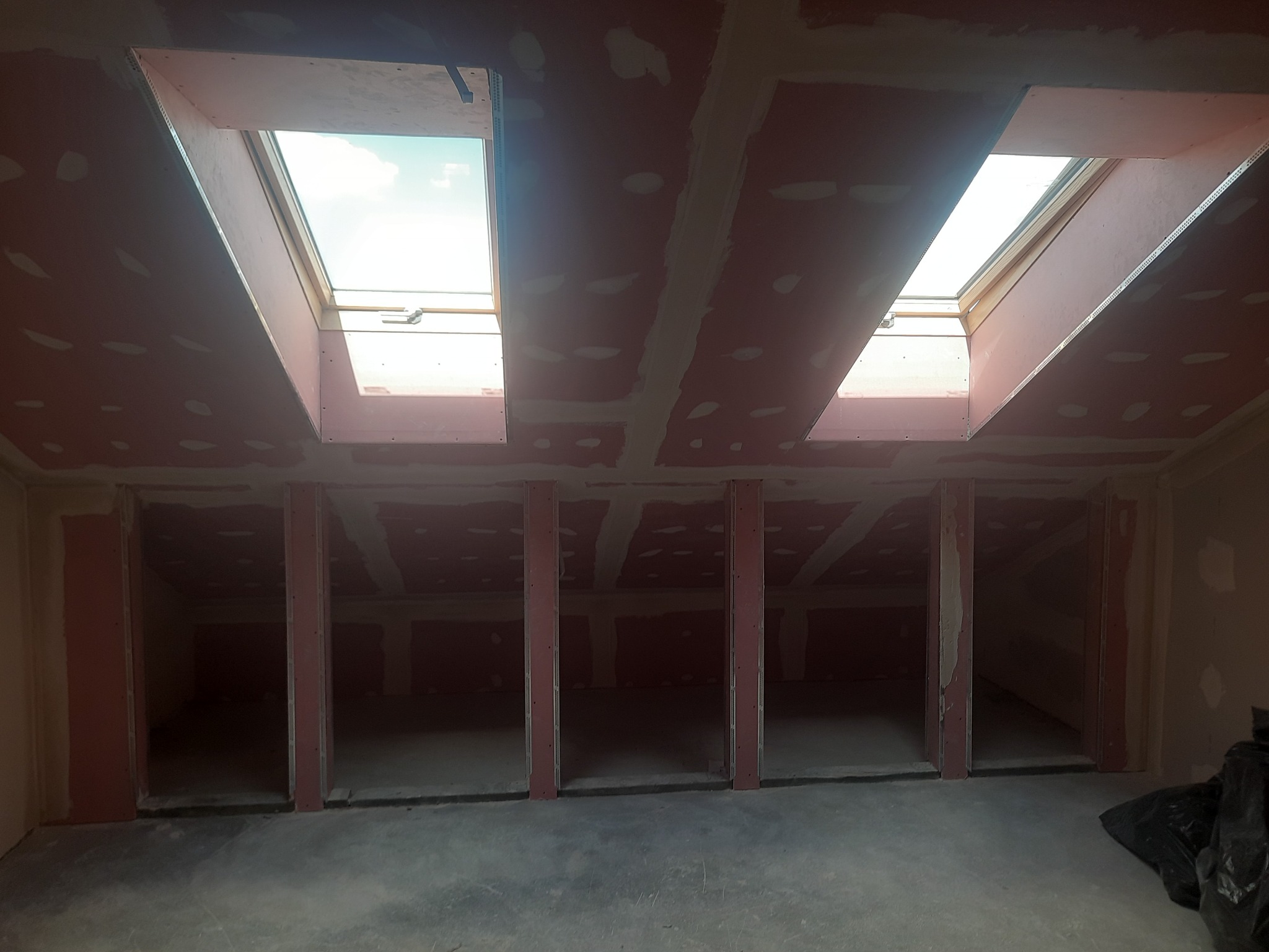 Montaż płyt w poddaszu z oknami dachowymi, widoczne spoiny wypełnione masą szpachlową, przygotowanie do dalszych prac wykończeniowych.