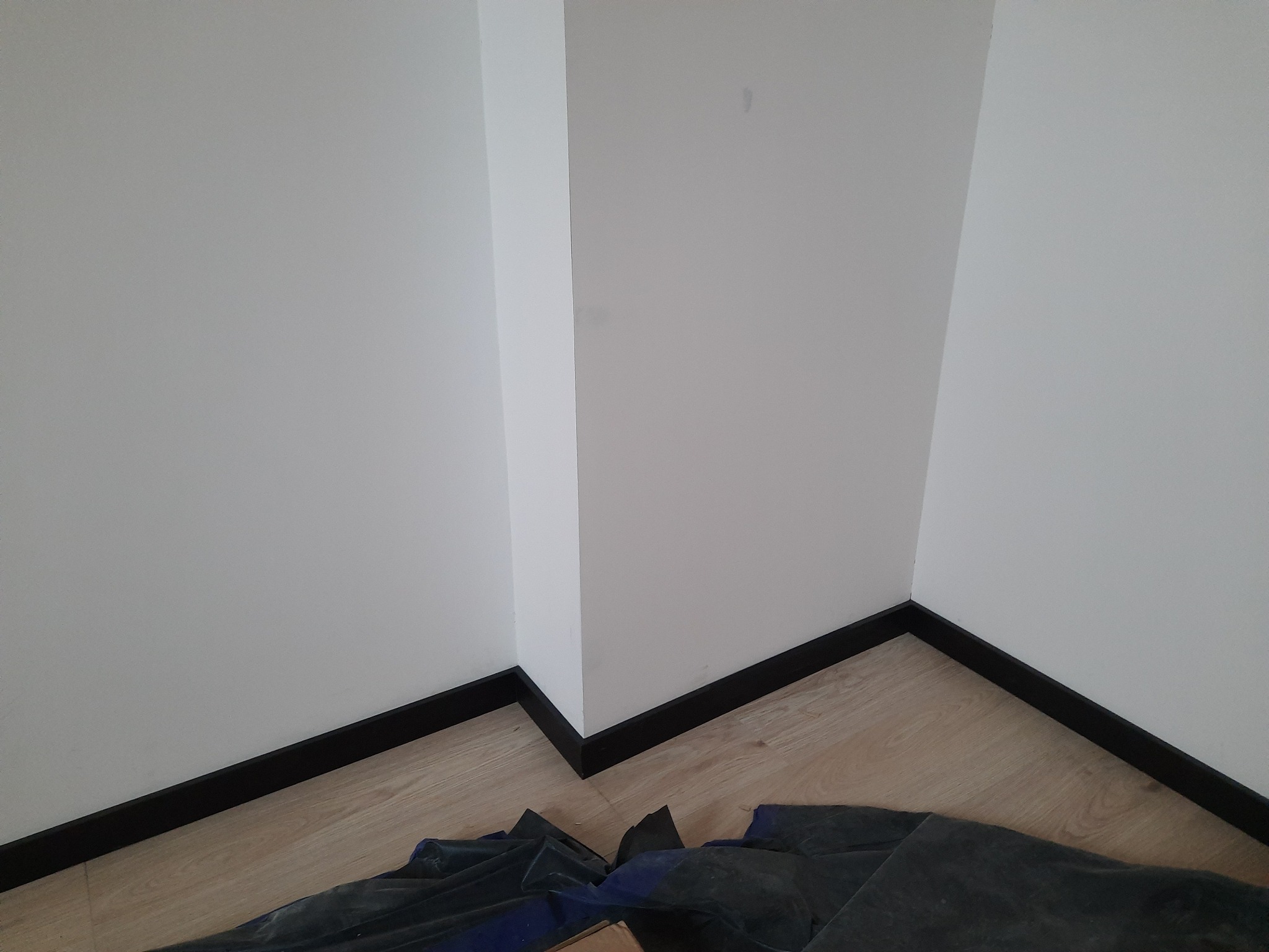 Wnętrze po świeżym malowaniu ścian na biało, z widocznymi czarnymi listwami przypodłogowymi i zabezpieczeniem podłogi folią malarską.