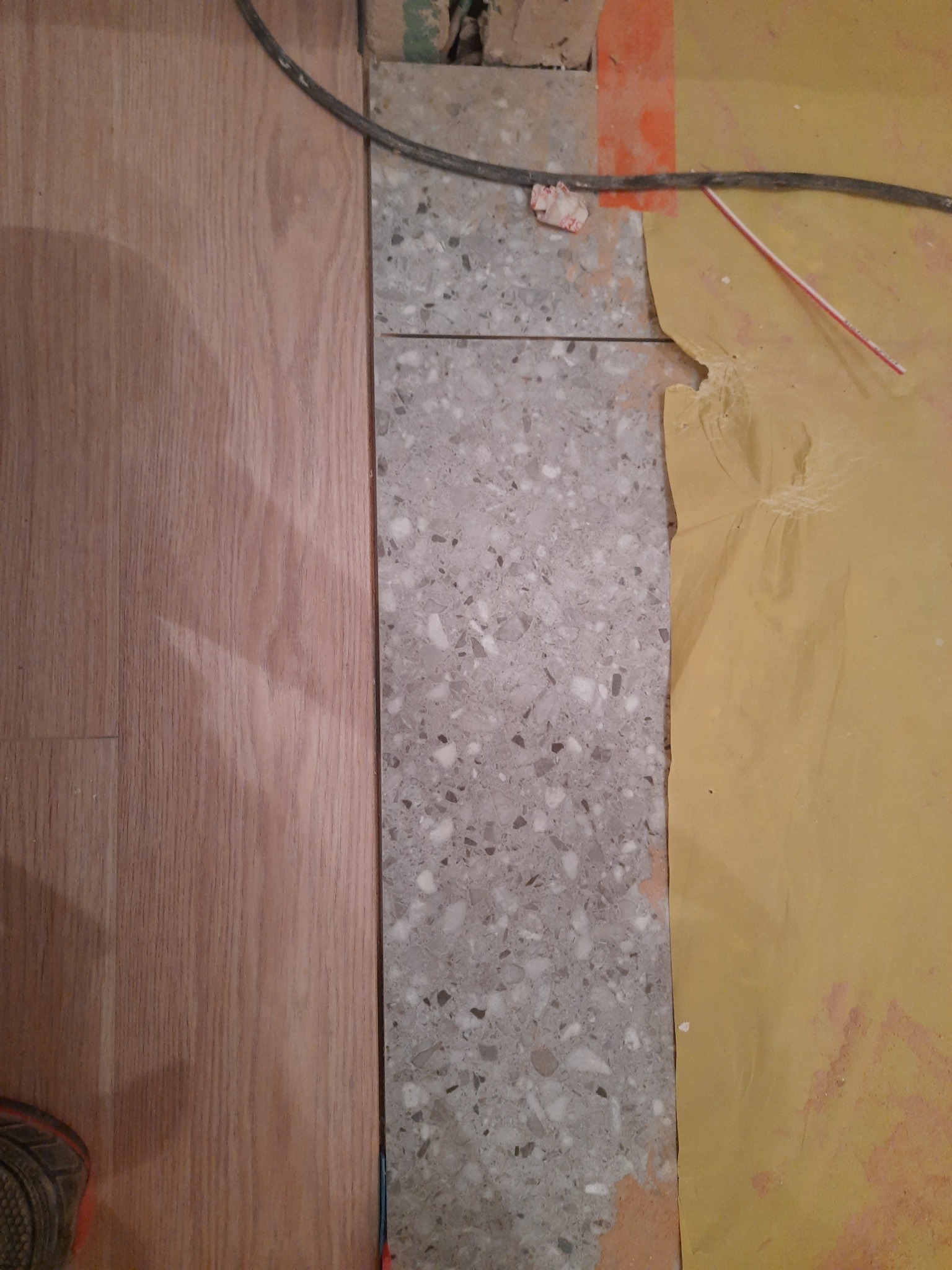 Fragment podłogi w trakcie remontu: świeżo położona drewniana podłoga sąsiaduje z fragmentem lastryko oraz zabezpieczoną folią ścianą.