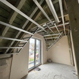 Oskar Romanowski - Adaptacja poddasza: metalowa konstrukcja sufitu podwieszanego na drewnianej więźbie, ściany częściowo wyszpachlowane, okno dachowe, narzędzia na podłodze.