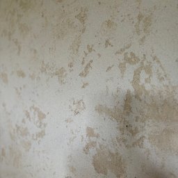 Oskar Romanowski - Niedokończona ściana z nierównomiernie nałożoną, jasną szpachlą, widoczne fragmenty starej warstwy, ujęcie z bliska pod kątem.