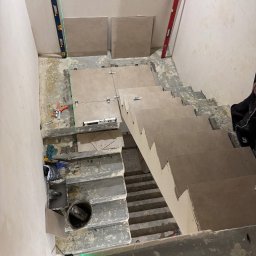 Oskar Romanowski - Montaż płytek na schodach z użyciem poziomicy laserowej. Widoczne płytki, poziomice, narzędzia glazurnicze i fragment schodów w trakcie wykańczania.