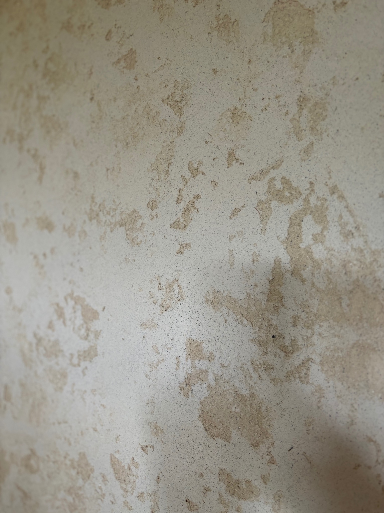 Niedokończona ściana z nierównomiernie nałożoną, jasną szpachlą, widoczne fragmenty starej warstwy, ujęcie z bliska pod kątem.