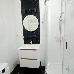 REM-TECH GRZEGORZ CICHY - Nowoczesna łazienka z czarno-białymi płytkami imitującymi marmur, okrągłym lustrem z oświetleniem punktowym, białą szafką pod umywalkę z drewnianymi akcentami i kabiną prysznicową z zaokrąglonymi...