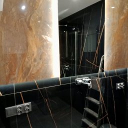 REM-TECH GRZEGORZ CICHY - Luksusowa łazienka z czarnymi płytkami imitującymi marmur ze złotymi żyłami, widoczne gniazdka elektryczne, drabinka i wiadro, odbicie kabiny prysznicowej w lustrze.