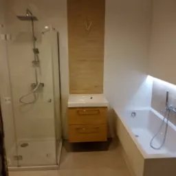 Nowoczesna łazienka z kabiną prysznicową typu walk-in, podświetlaną wanną i szafką z umywalką z drewnianym frontem, wykończona w jasnych, neutralnych kolorach.