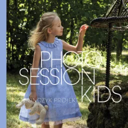 Dziewczynka w błękitnej sukience z pluszowym króliczkiem dotyka ręką metalowej konstrukcji na tle zieleni.