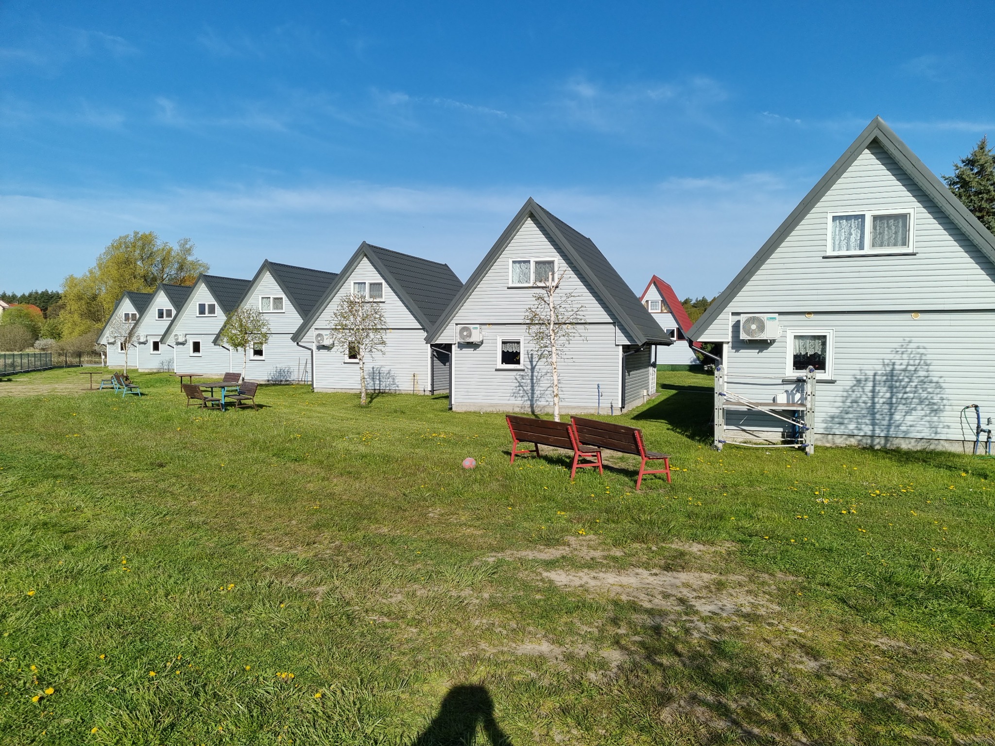 Rząd identycznych domków letniskowych z klimatyzatorami na ścianach, ustawionych na trawniku pod błękitnym niebem.