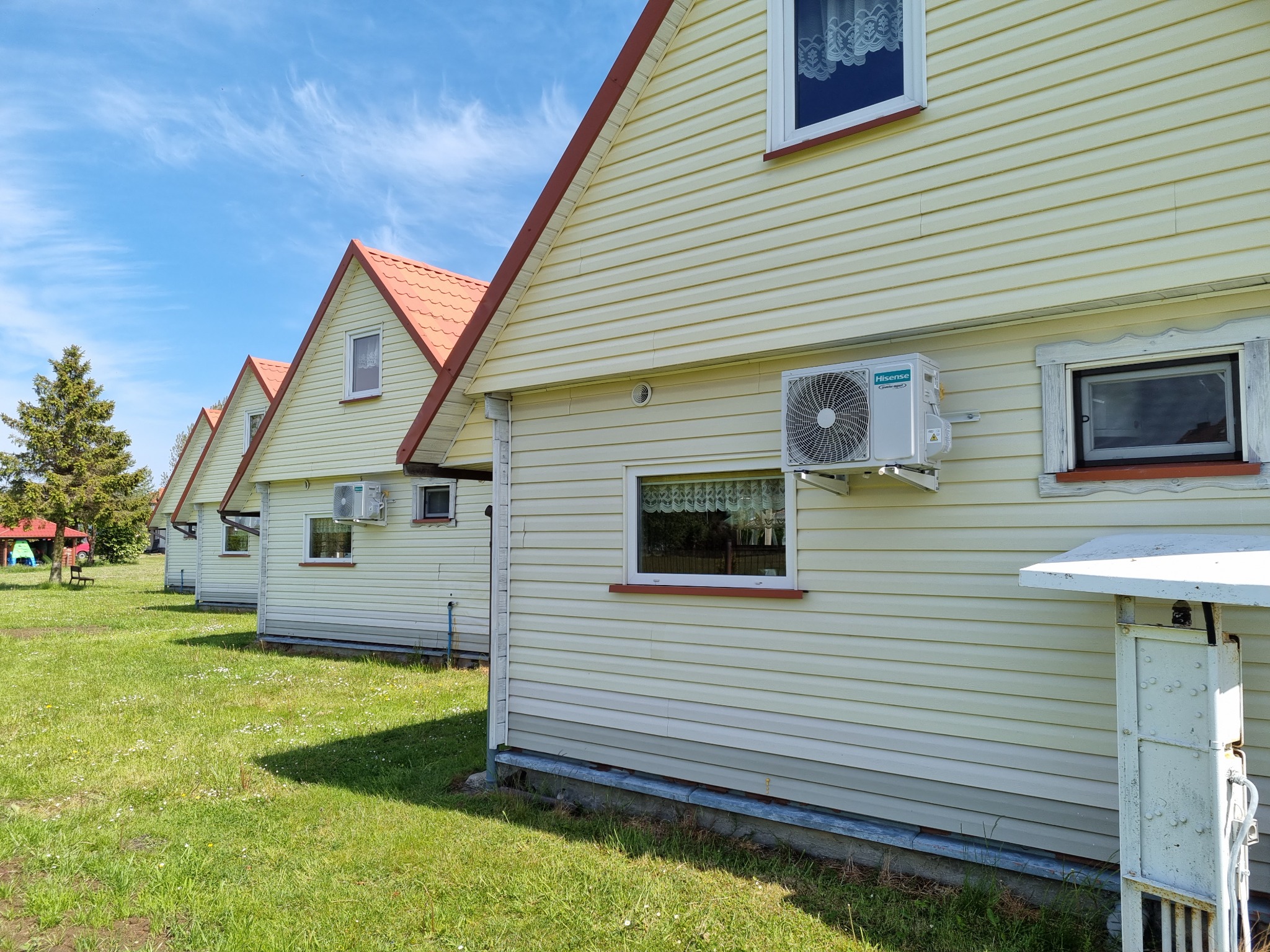 Szereg domków letniskowych z zamontowaną klimatyzacją Hisense na elewacji w słoneczny dzień w okolicach Poznania. Widoczna trawa i błękitne niebo.
