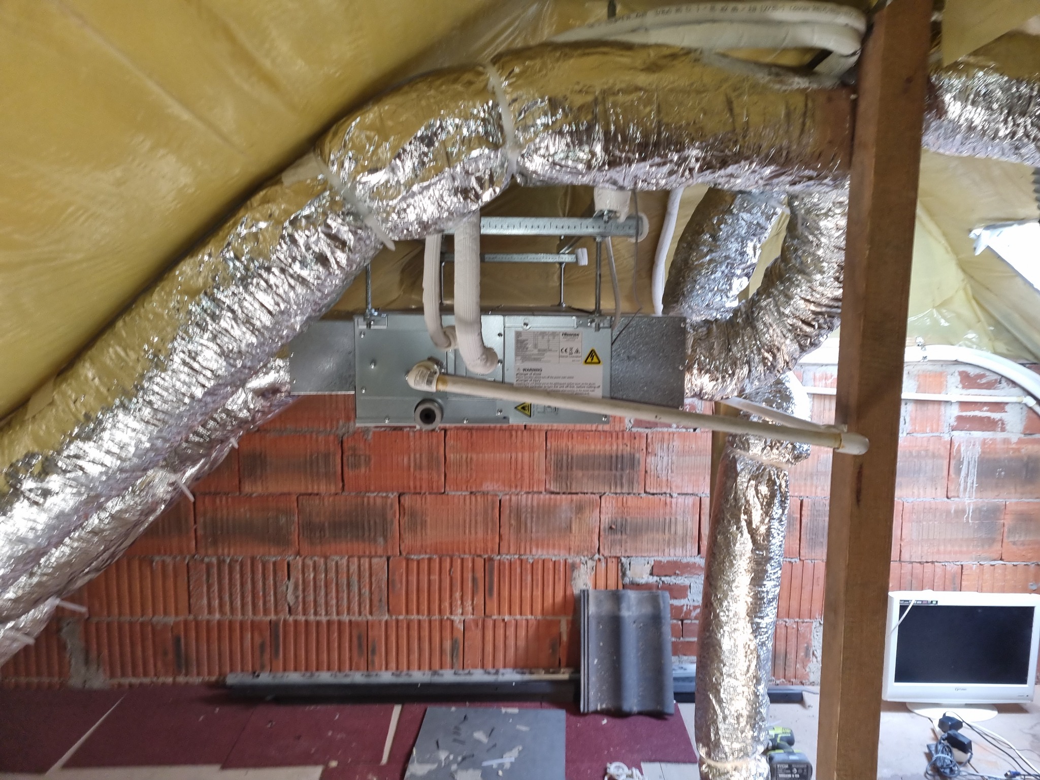 Montaż centrali wentylacyjnej z rurami spiro w przestrzeni poddasza z widoczną ceglaną ścianą i ociepleniem dachu.