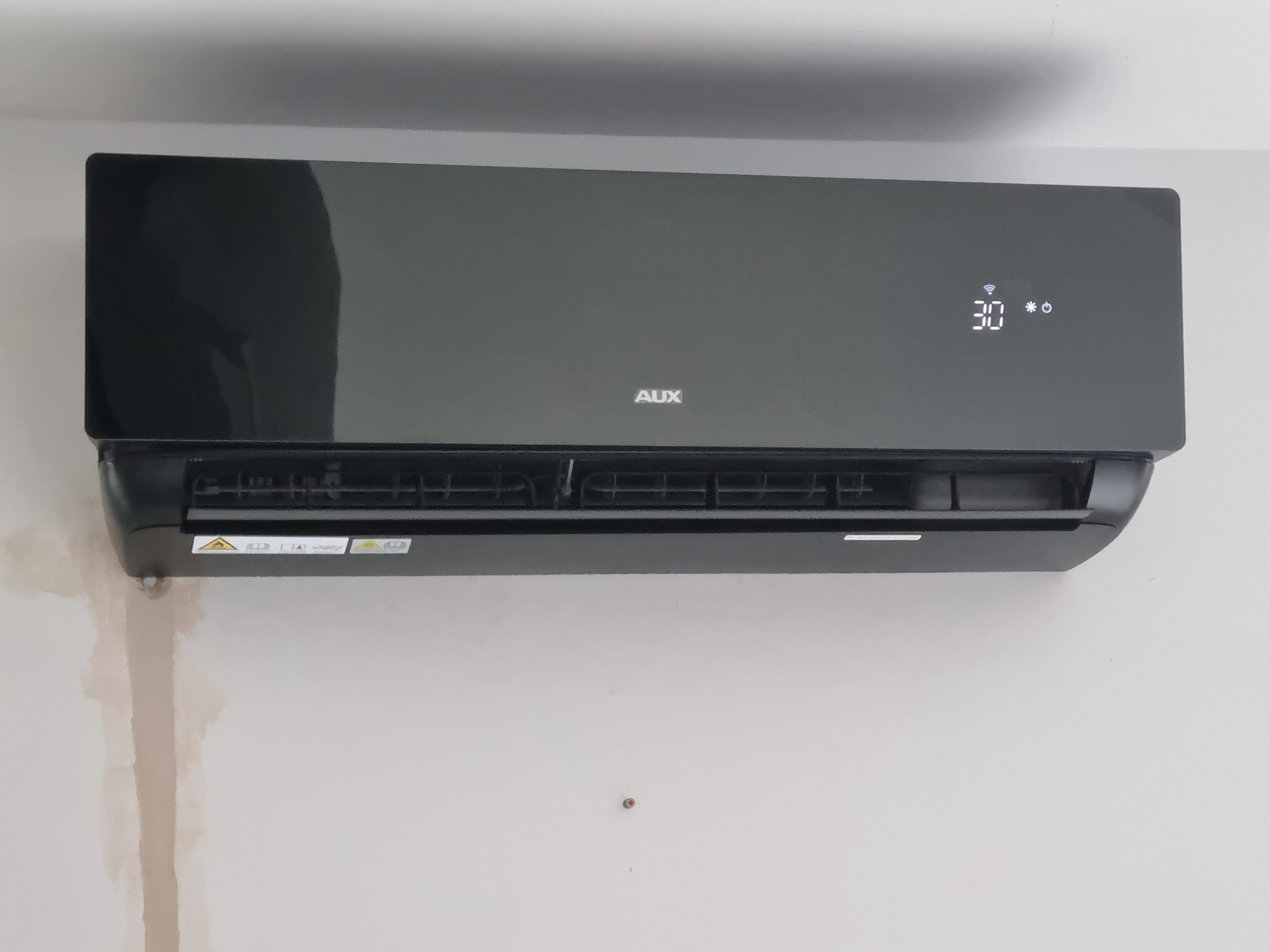 Czarna klimatyzacja AUX zamontowana na białej ścianie, widoczne ślady po montażu.