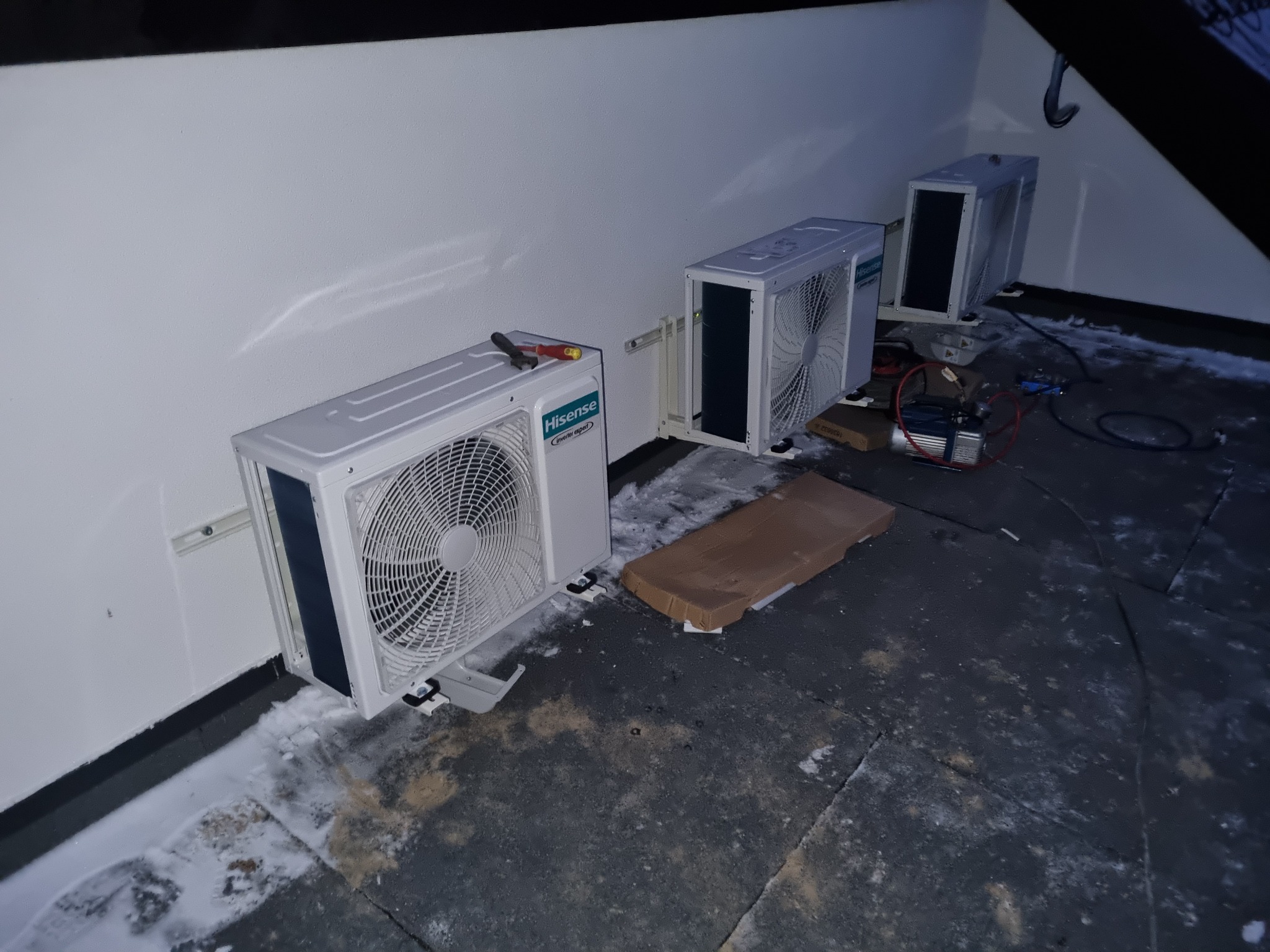 Trzy białe jednostki zewnętrzne klimatyzacji Hisense zamontowane na dachu, widoczny sprzęt serwisowy i narzędzia, instalacja w trakcie prac.