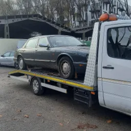 Szary Jaguar XJ na lawecie w Wągrodnie, widok z boku, w tle budynki i drzewa.
