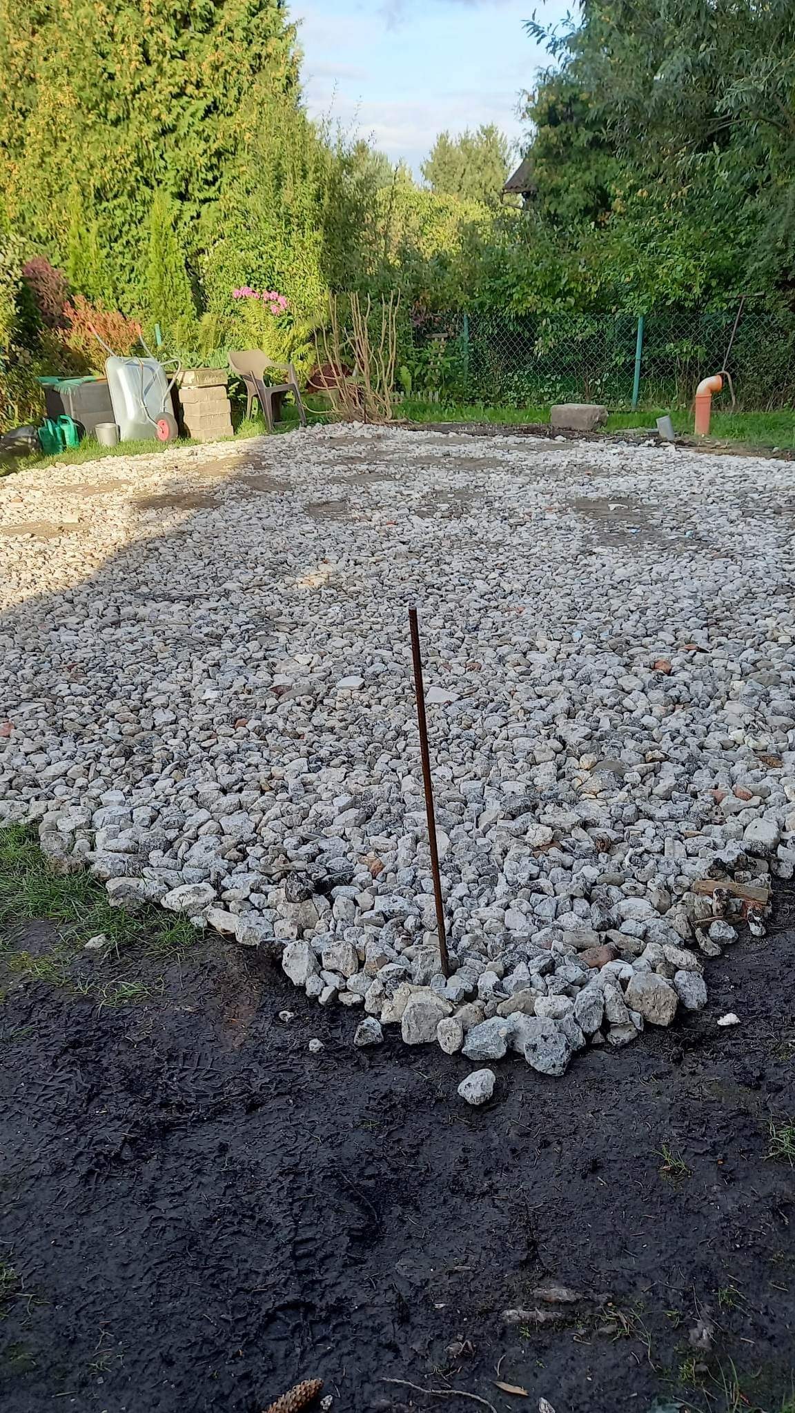 Przygotowany teren pod trawnik z wysypanym żwirem, widoczna ubita ziemia na obrzeżach i w tle zieleń ogrodu.